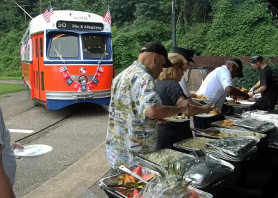BBQ attendees line up at the buffet table to fill their plates with an assortment of outstanding choices as PCC No.2168, built by the St. Louis Car Company in 1948, looks on.